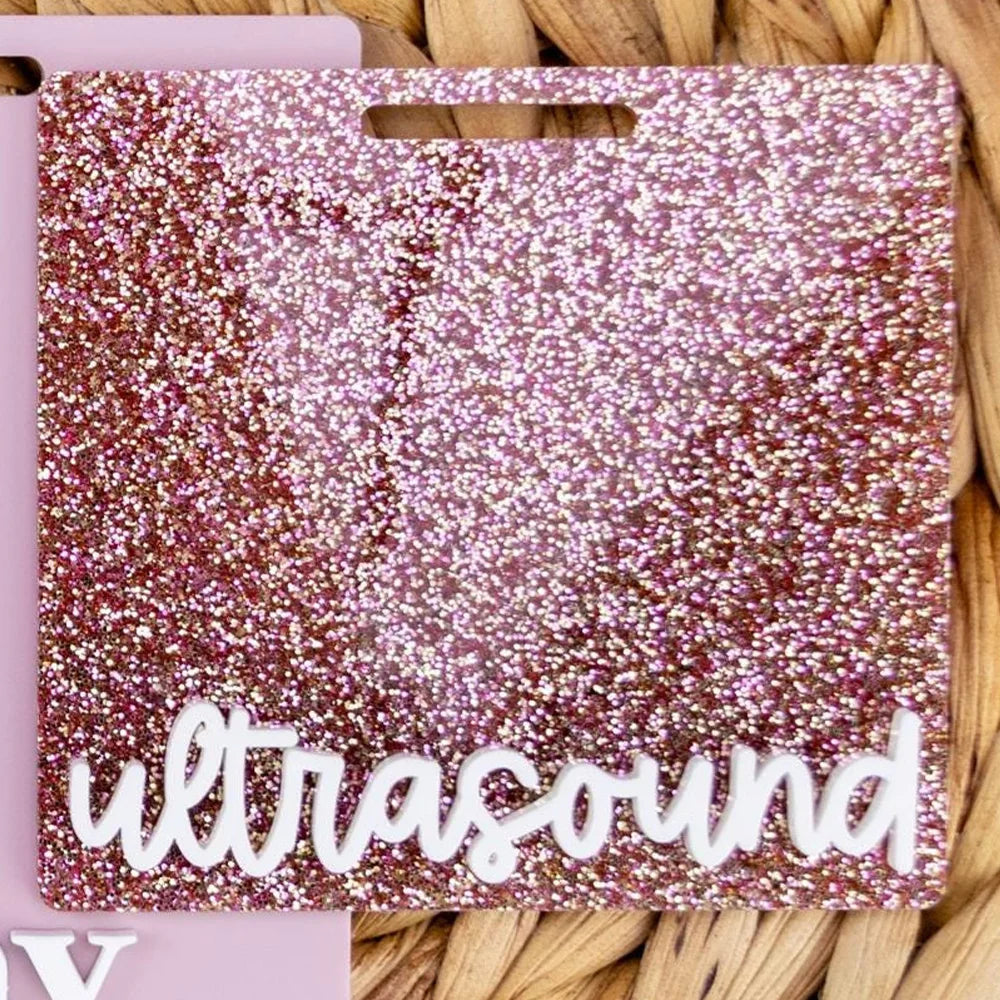 A square acrylic badge holder with a glittery magenta background and the word ultrasound written in white script.