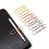 A set of mixed color heart-shaped metal pen clips arranged on a black leather surface.