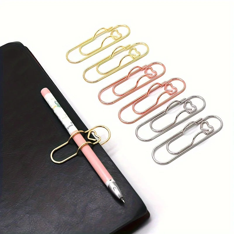 A set of mixed color heart-shaped metal pen clips arranged on a black leather surface.