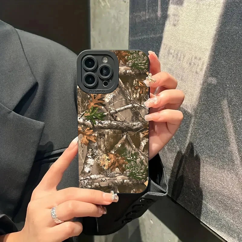 Une main tient un iPhone avec une coque silicone camouflage de forêt, représentant des branches et des feuilles d'arbres.
