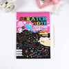 A pink spiral notebook titled Scratch Note with colorful drawings and text, next to a pink cosmetic item.