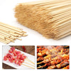 A large bundle of natural bamboo skewers and a plate of cooked meat on skewers.