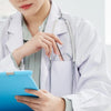 A person in a white lab coat is writing or taking notes with a blue tablet while holding a pen.