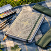 A5 dot grid notebook with a botanical design and gold foil accents resting on a blue plaid fabric.