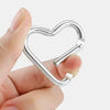 A hand holds a silver heart-shaped spring clasp and carabiner keychain.