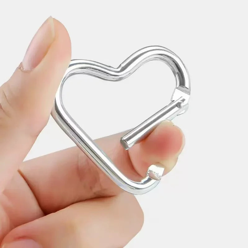 A hand holds a silver heart-shaped spring clasp and carabiner keychain.