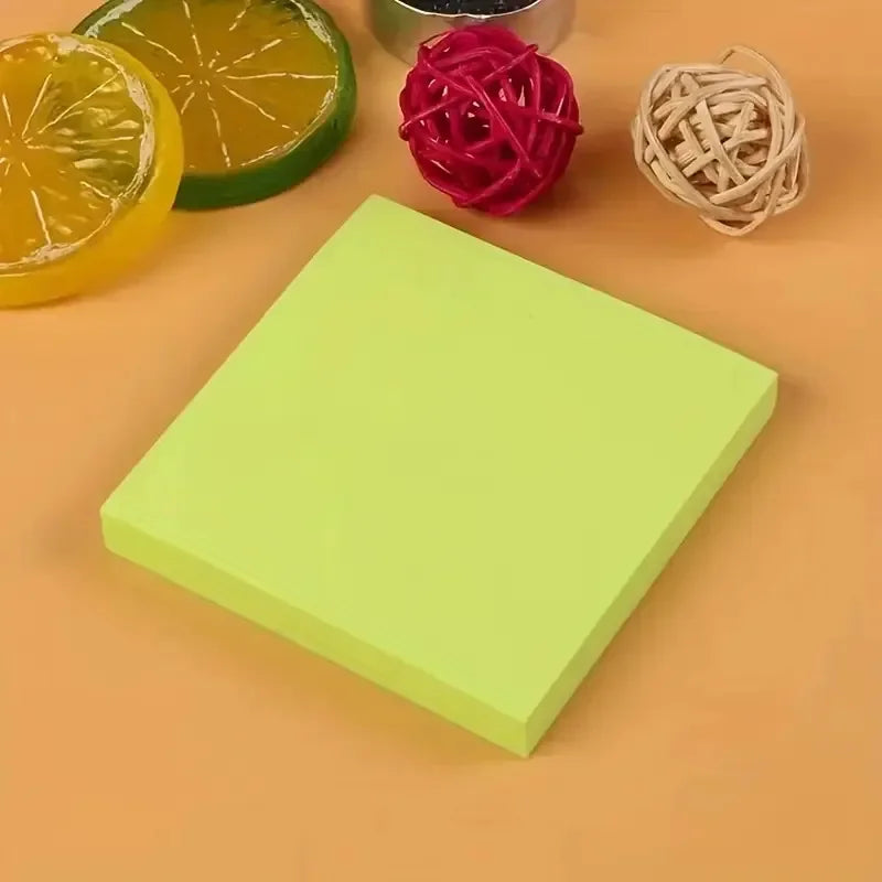 A stack of vibrant neon self-adhesive sticky notes in lime green and pink, next to a slice of orange and some twine.