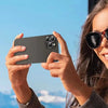 Eine Frau hält ein dunkles Smartphone mit Schutzglas bei blauem Himmel.