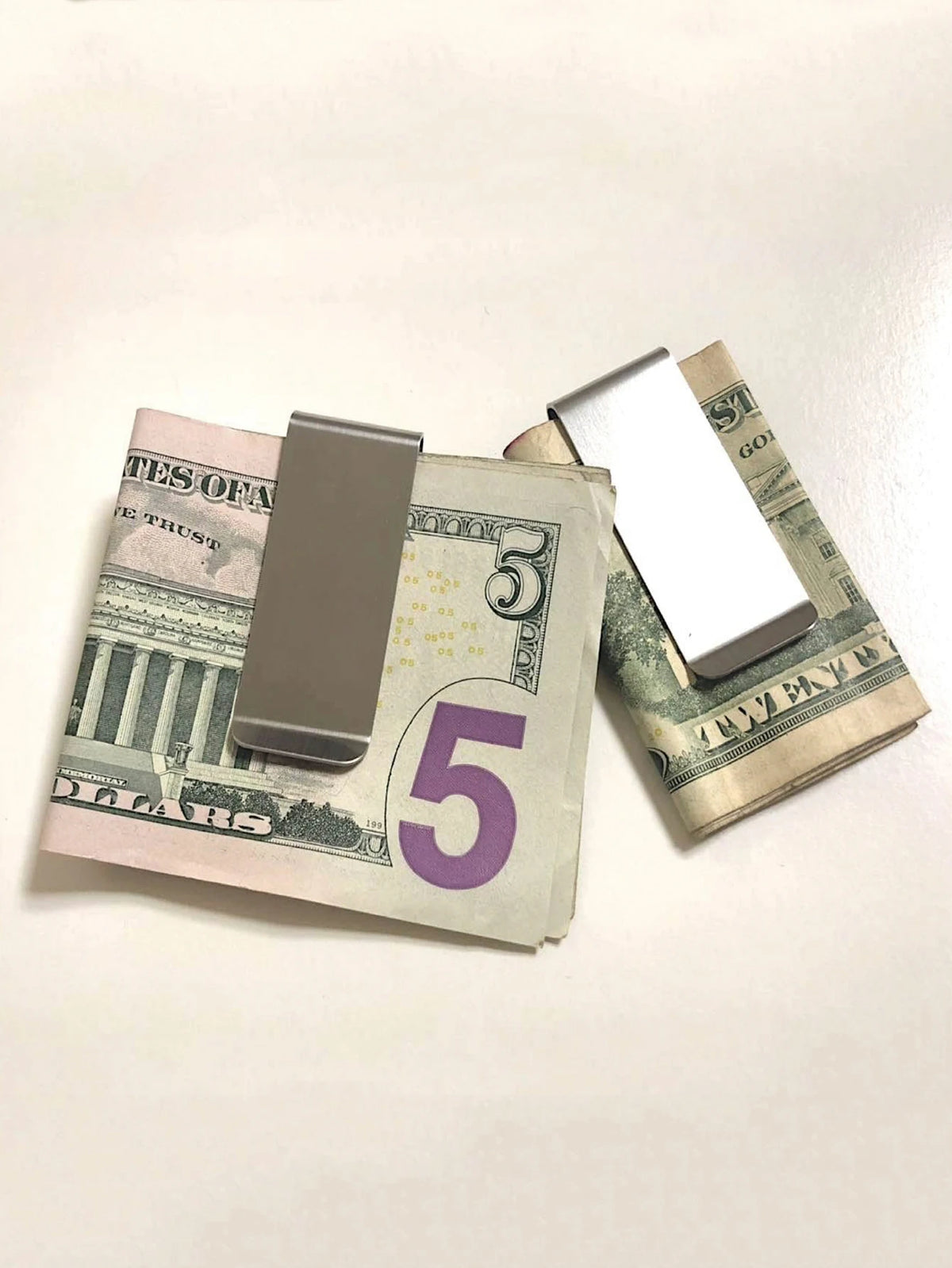A stainless steel money clip resting on top of a five dollar bill.