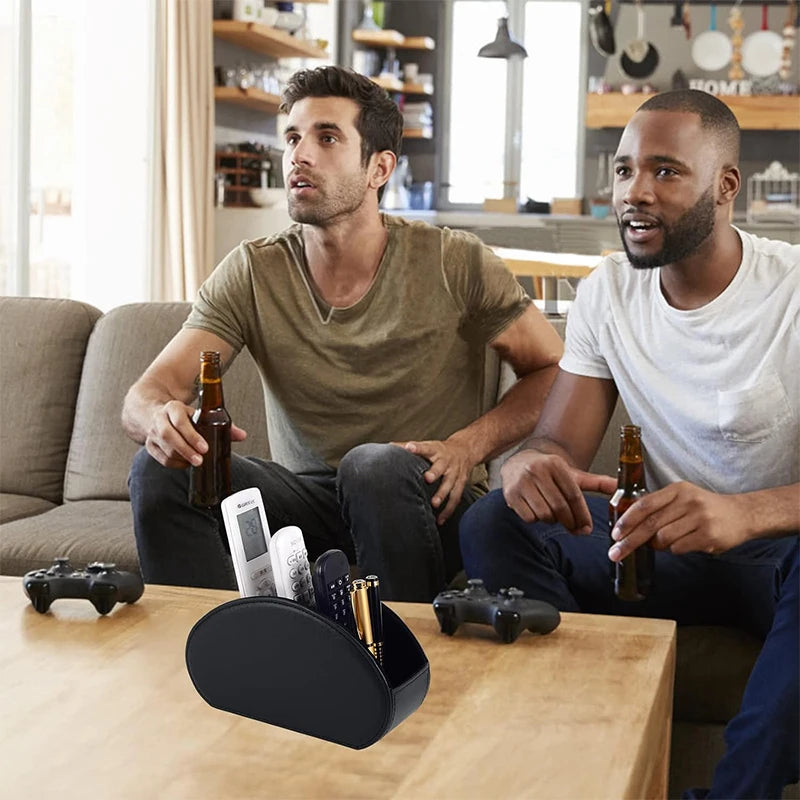 A man is sitting at a wooden table with a PU leather remote caddy organizer and a game controller.