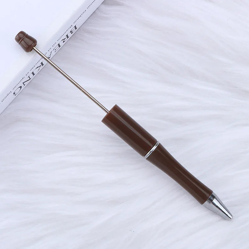 A brown DIY beadable pen with a silver tip rests on a white, fluffy surface next to a ruler.