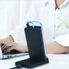 A black magnetic foldable wireless charging stand is shown next to a laptop on a white surface.