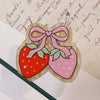 A set of ten pink and red strawberry-shaped acrylic hairbows with a bow detail resting on aged paper.