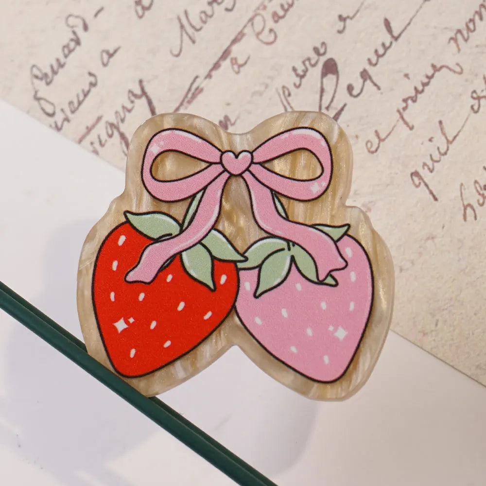 A set of ten pink and red strawberry-shaped acrylic hairbows with a bow detail resting on aged paper.