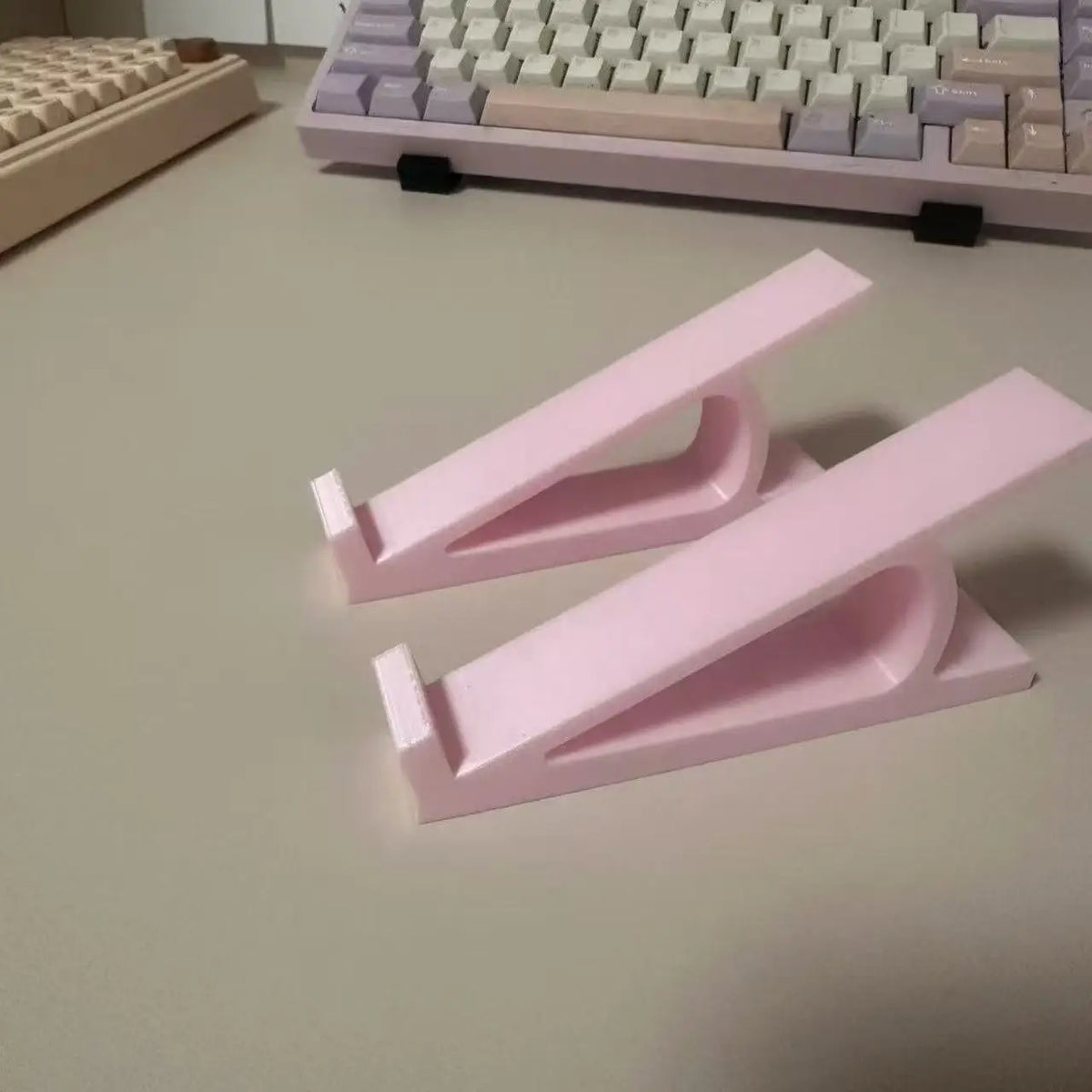 Rosa ergonomische Tastatur-Höhenverstellvorrichtung mit zwei verstellbaren Stützen auf einer hellen Oberfläche.