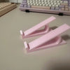 Pinker ergonomischer Tastaturhöhenverstellbarer Ständer mit zwei verstellbaren Haltern auf einer hellen Oberfläche.