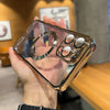 A hand holds a clear magnetic phone case with a gold plated finish, displaying the MagSafe ring and multiple magnetic attachm