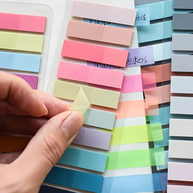 A hand is placing a yellow tab onto a colorful set of fluorescent transparent organization markers.