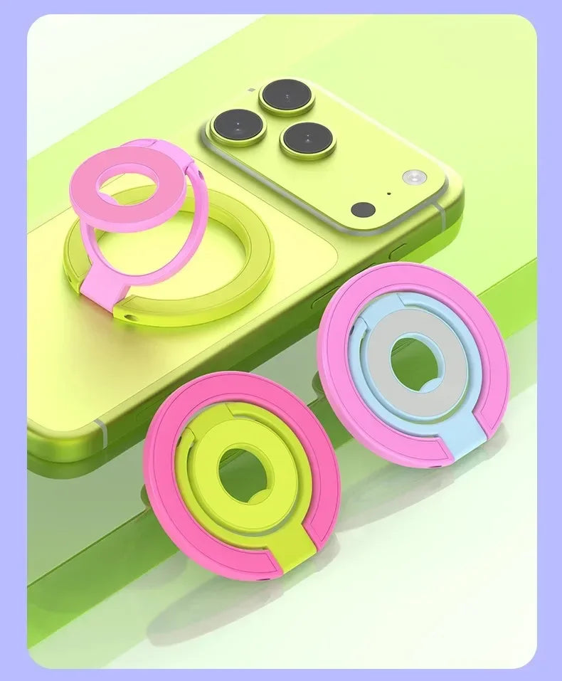 A pink and lime green magnetic ring grip with a foldable kickstand shown next to a yellow MagSafe phone.