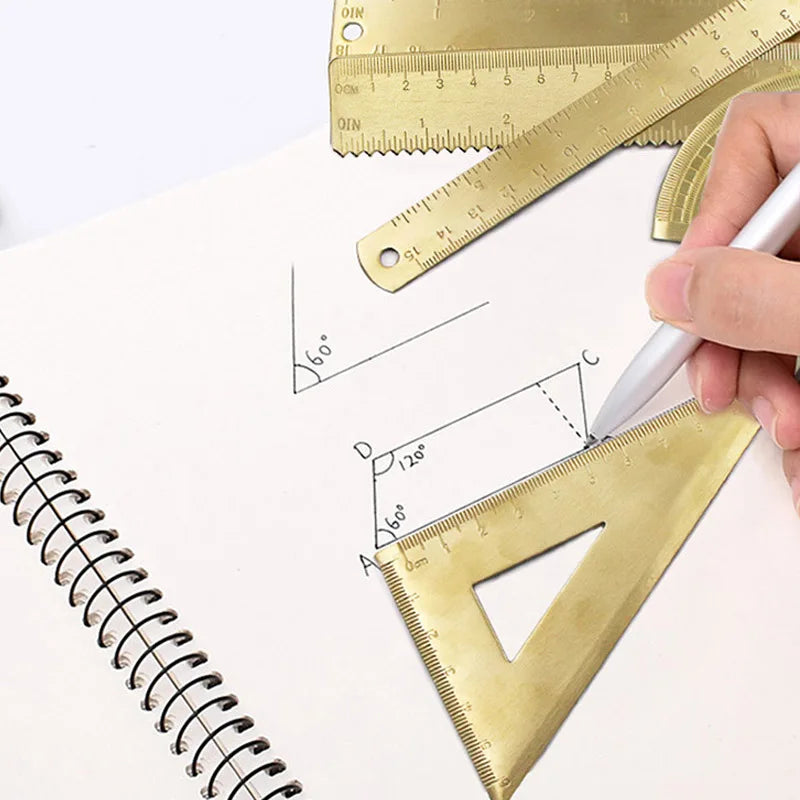 A hand uses a brass drafting set ruler to measure and draw angles on a sheet of paper.