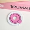 A pink magnetic phone grip and stand with a foldable ring is shown on a white surface.
