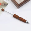 A long, silver pen accessory with a gold-colored beaded tip rests on a white surface next to a wooden frame.