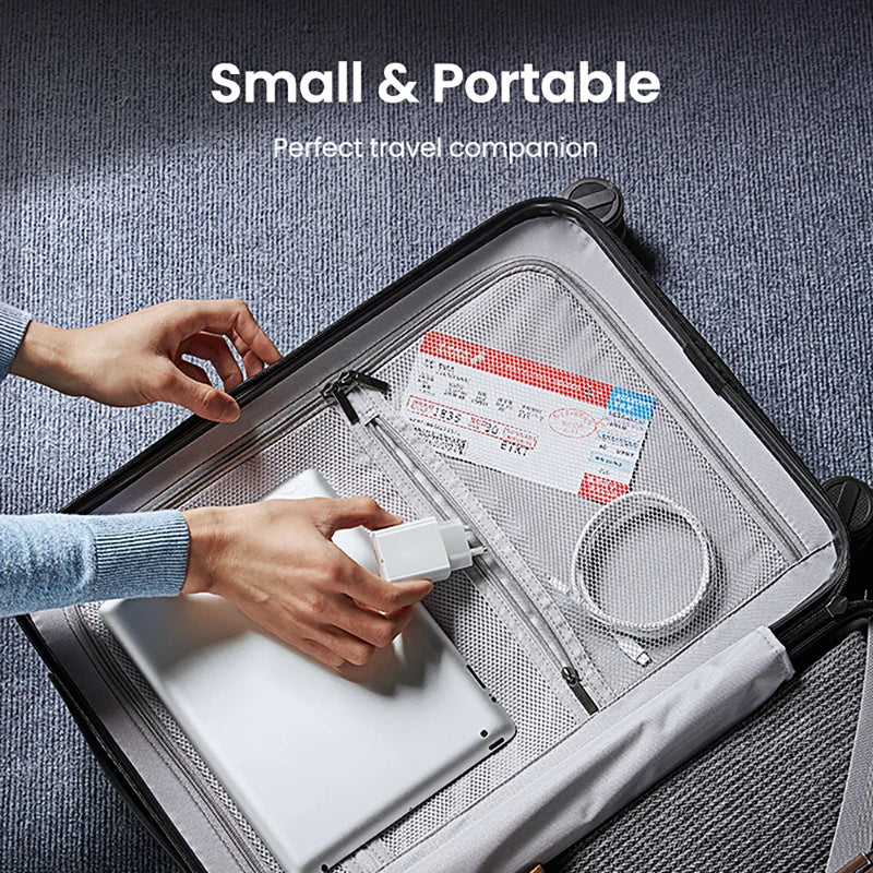 A hand is placing a white laptop into a gray portable backpack alongside a 30W USB-C fast charger and cable.