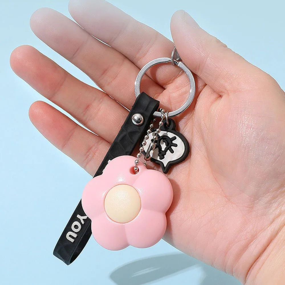 A hand holds a silver ring with a black leather strap and a pink flower charm for a floral design letter opener and paper cut