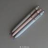 A collection of precision gel pens in various sizes and colors, including pink, gray, and blue, displayed diagonally on a neu