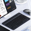 A black multi-device Bluetooth keyboard and mouse combo placed on a white desk next to a laptop and a cup.