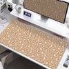 A large leopard print desk pad is displayed on a white desk next to a computer monitor and other office supplies.