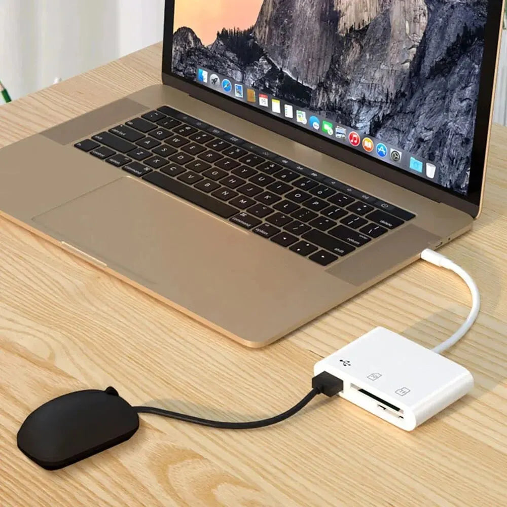 A laptop displaying a scenic image is shown next to a white memory card reader and adapter on a wooden table.