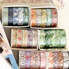 A collection of five rolls of floral patterned washi tape in various colors and designs displayed in white containers.