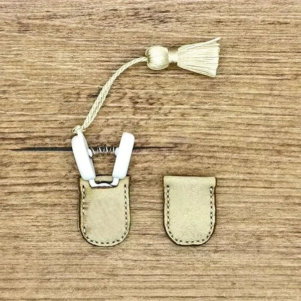 Mini sewing scissors with white handles and a gold-colored tassel resting on a wooden surface.