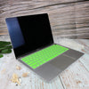 A silver silicone keyboard cover for a MacBook, shown open on a light wooden surface.
