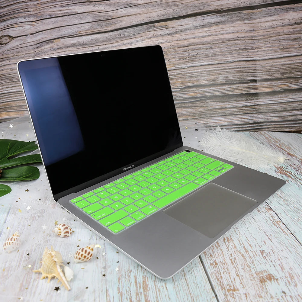 A silver silicone keyboard cover for a MacBook, shown open on a light wooden surface.