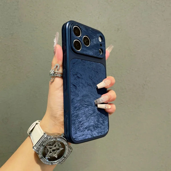 A hand holds a dark blue phone case with a frosted velvet texture and gold accents against a gray background.