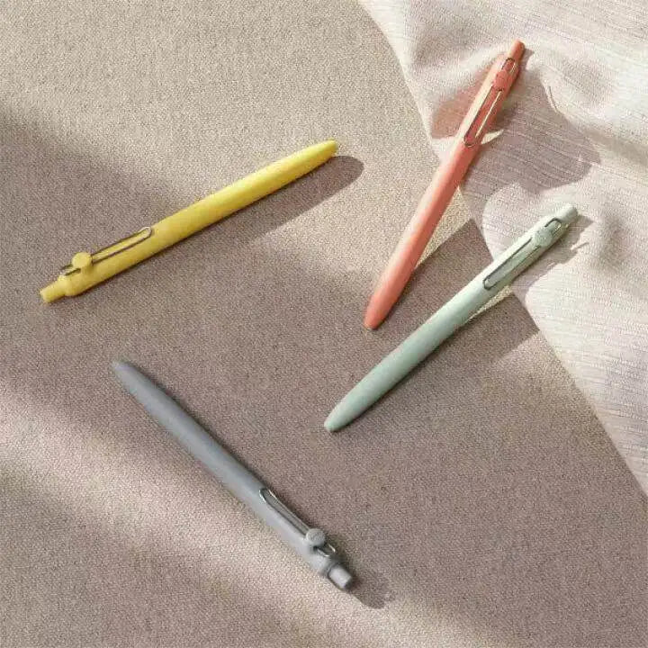 Three precision gel pens in yellow, pink, and gray lying on a light beige fabric.