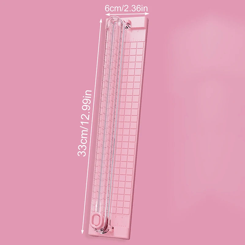 A pink portable manual paper cutter trimmer with a scale marked in centimeters and inches.
