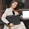 A woman is holding a black protective laptop sleeve bag with reinforced padding in a light beige blazer.