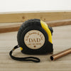 A black and yellow measuring tape is shown next to a brass tube on a wooden surface.