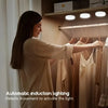 A woman is adjusting clothes on a wooden rack under automatic induction lighting in a closet.