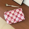 A pink floral quilted ladies clutch purse resting on a wooden surface next to a makeup brush.