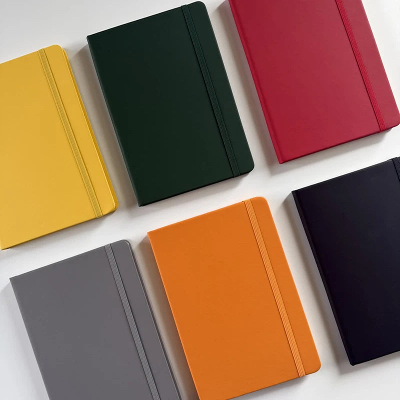 A collection of five A5 hardcover lined notebooks in yellow, dark green, red, orange, and gray.