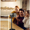 A Cooper ChatStand phone tripod stand is shown on a wooden table with people interacting in the background.