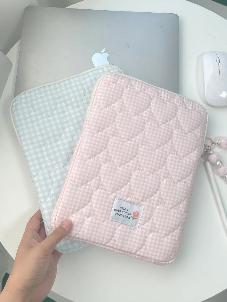 A pink quilted laptop sleeve with a light blue checkered lining is shown next to a silver Apple laptop.