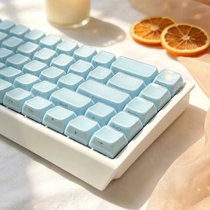 A close-up of light blue crystal jelly side-printed keycaps for a mechanical keyboard resting on a white surface with an oran