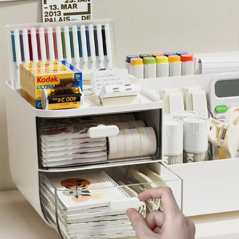 A white desk organizer with two clear storage drawers holds various pens, paper, and office supplies.