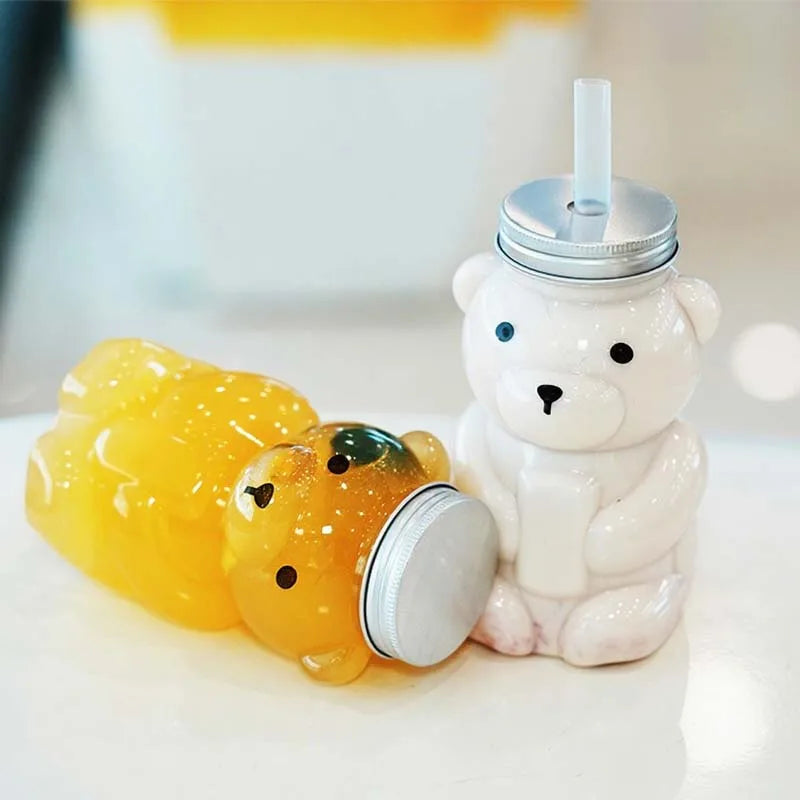 A white bear-shaped reusable water bottle next to a yellow, bear-shaped silicone cup.