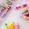A collection of cute cartoon mini ballpoint pens in various colors and designs laid out on a white grid paper.